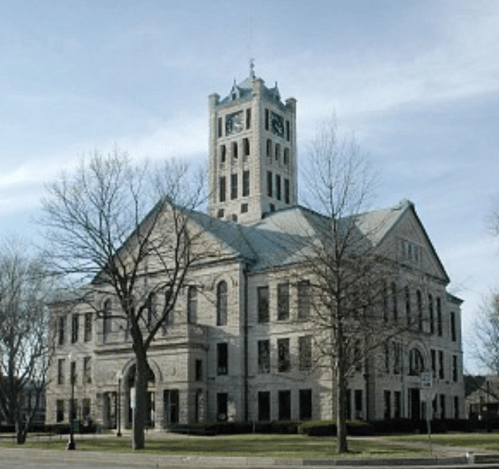 Historic stone building with a clock tower, surrounded by bare trees and a clear sky.